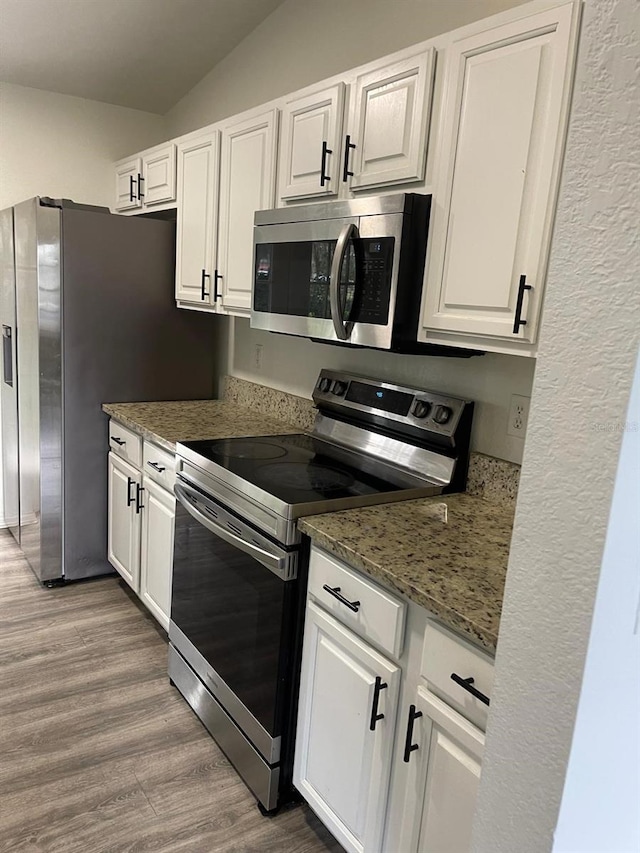 kitchen featuring hardwood / wood-style floors, vaulted ceiling, dark stone countertops, appliances with stainless steel finishes, and white cabinetry