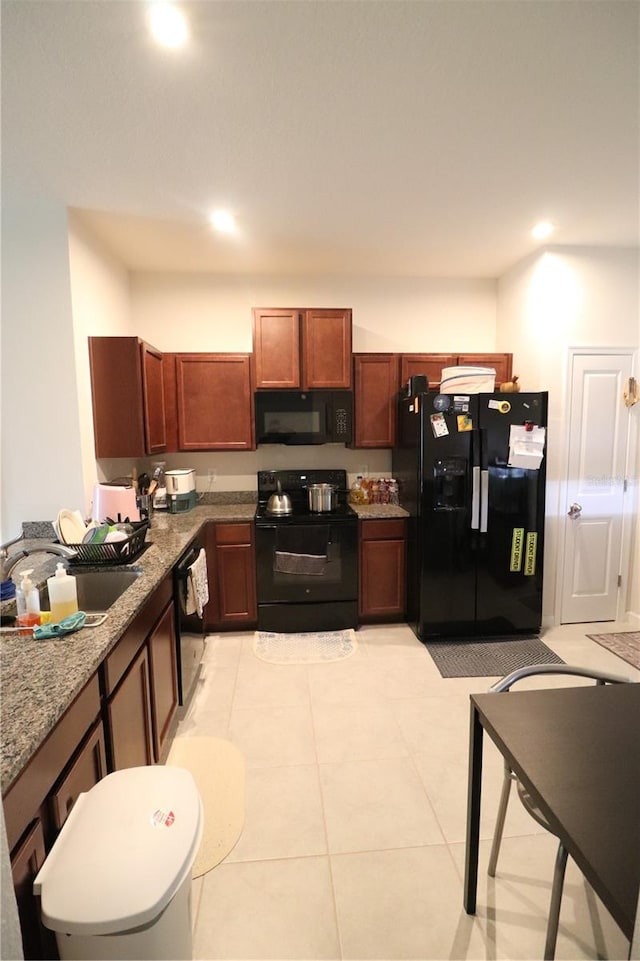 kitchen featuring dark stone counters, sink, light tile floors, and black appliances