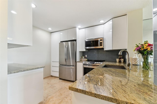 kitchen with white cabinets, stainless steel appliances, kitchen peninsula, and light stone countertops