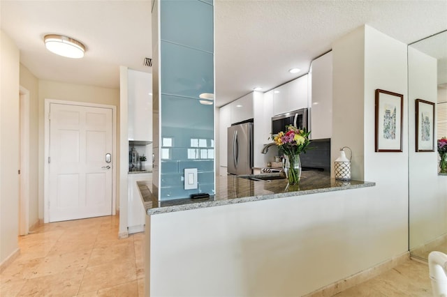 kitchen featuring appliances with stainless steel finishes, white cabinetry, kitchen peninsula, a textured ceiling, and dark stone counters