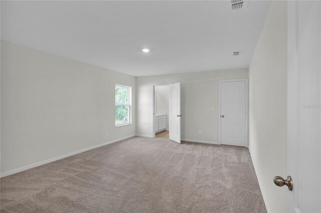 unfurnished bedroom featuring ensuite bath and light colored carpet