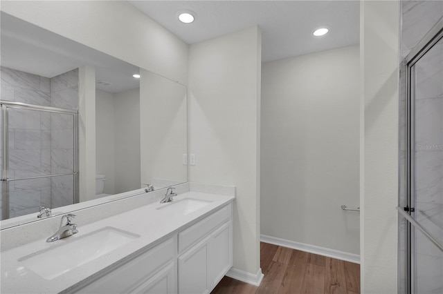 bathroom with toilet, vanity with extensive cabinet space, wood-type flooring, dual sinks, and an enclosed shower