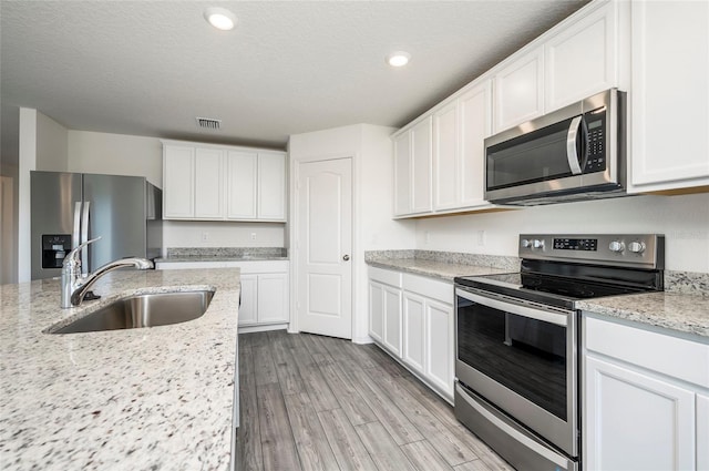 kitchen with white cabinets, light stone countertops, light hardwood / wood-style flooring, sink, and stainless steel appliances