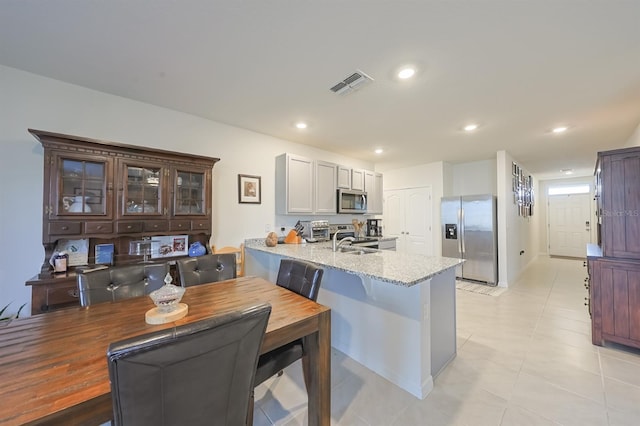 kitchen featuring stainless steel appliances, sink, light stone counters, kitchen peninsula, and light tile patterned flooring