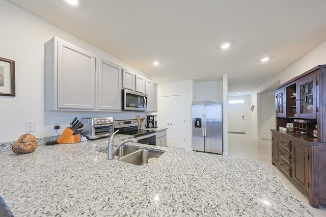 kitchen with light tile patterned floors, appliances with stainless steel finishes, sink, and light stone countertops