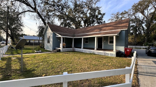 view of front facade featuring a porch, roof with shingles, fence, and a lawn