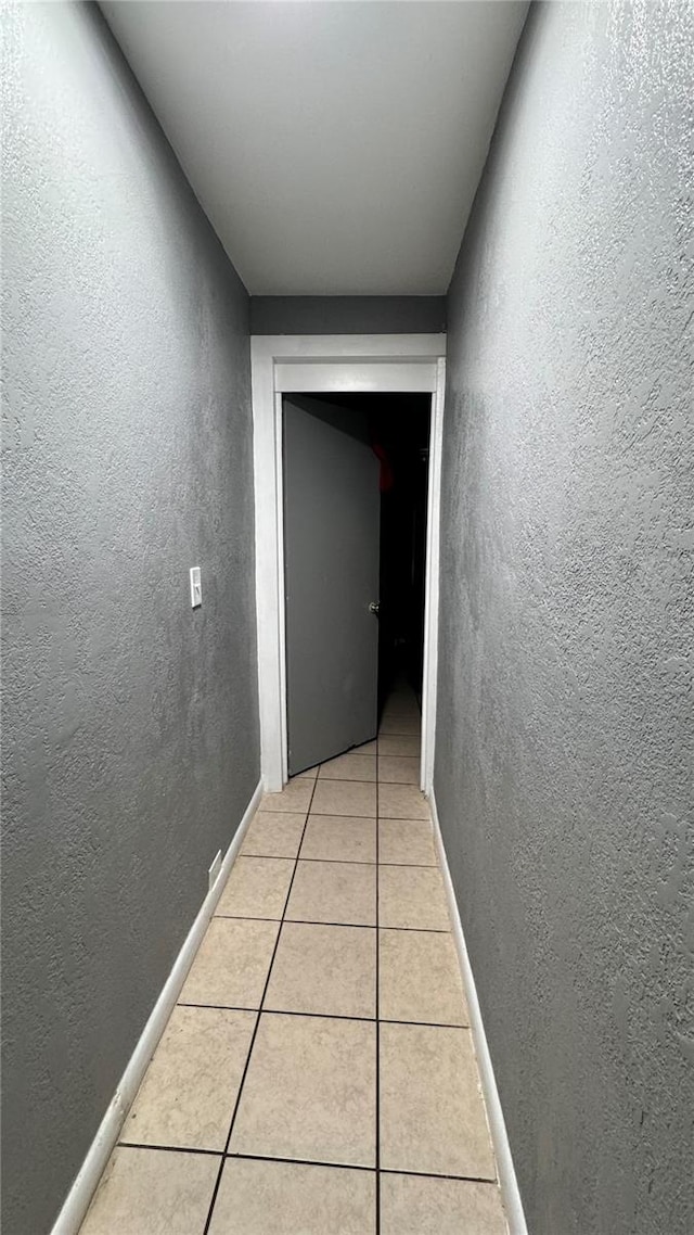 hall featuring a textured wall, baseboards, and light tile patterned floors
