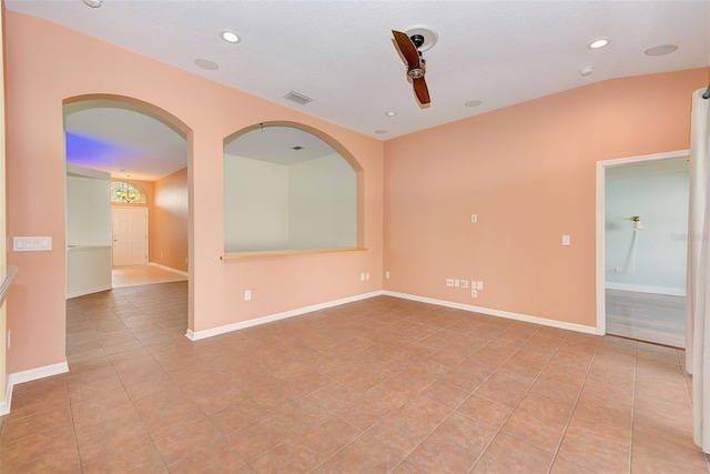 empty room with a textured ceiling, lofted ceiling, ceiling fan, and light tile flooring