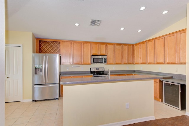 kitchen featuring stainless steel appliances, light tile flooring, vaulted ceiling, beverage cooler, and a kitchen island with sink