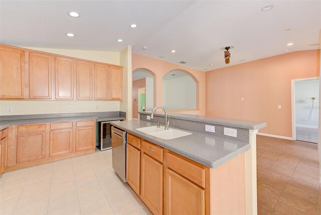 kitchen with an island with sink, sink, light tile floors, stainless steel dishwasher, and vaulted ceiling