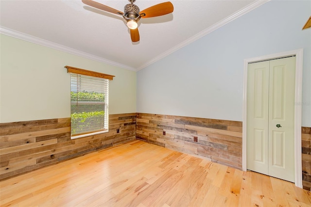 spare room with wood walls, ornamental molding, ceiling fan, and light wood-type flooring