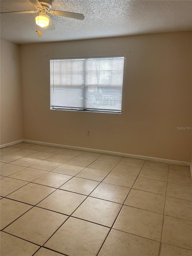 spare room with a textured ceiling, ceiling fan, light tile floors, and a wealth of natural light