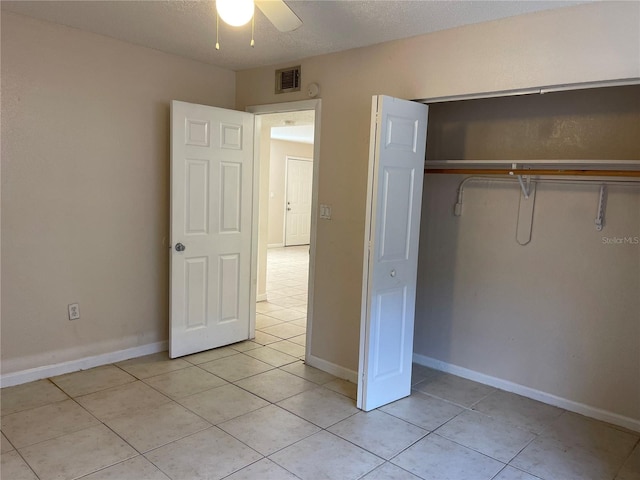 unfurnished bedroom featuring light tile flooring, a closet, ceiling fan, and a textured ceiling