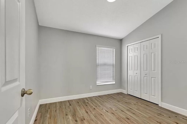 unfurnished bedroom with vaulted ceiling, a closet, and light wood-type flooring