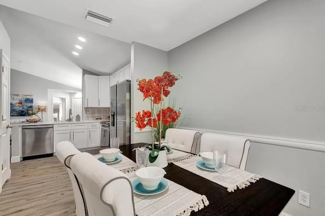 dining room with lofted ceiling, light wood-type flooring, and sink