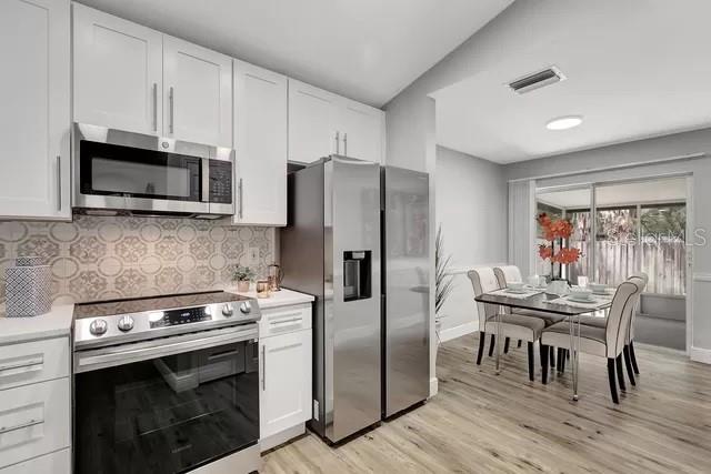 kitchen featuring lofted ceiling, white cabinetry, backsplash, appliances with stainless steel finishes, and light wood-type flooring