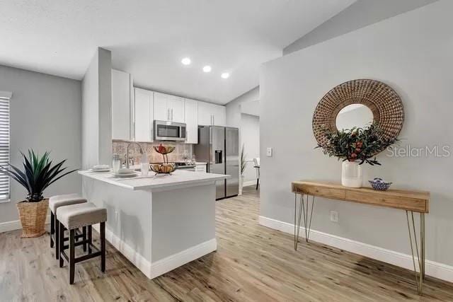 kitchen featuring white cabinets, a breakfast bar, light hardwood / wood-style floors, stainless steel appliances, and lofted ceiling