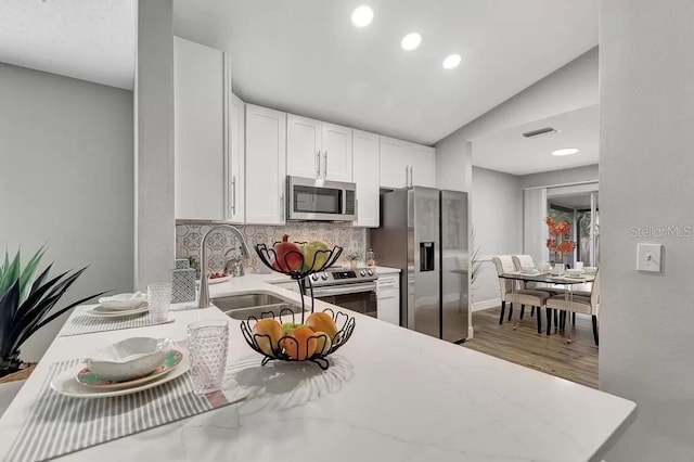 kitchen featuring white cabinets, light hardwood / wood-style flooring, backsplash, stainless steel appliances, and vaulted ceiling