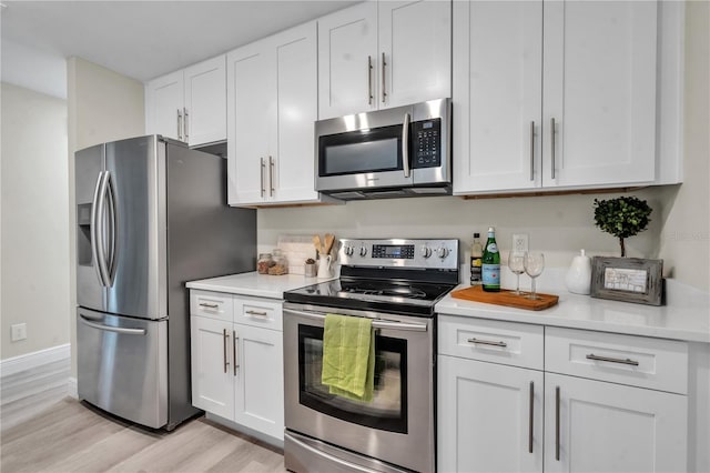 kitchen with stainless steel appliances, white cabinetry, and light hardwood / wood-style flooring