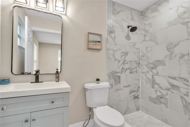 bathroom with toilet, a tile shower, and vanity