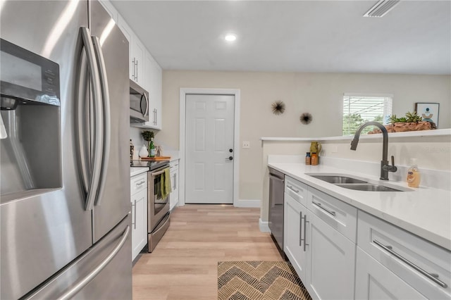 kitchen with sink, white cabinets, appliances with stainless steel finishes, and light hardwood / wood-style flooring