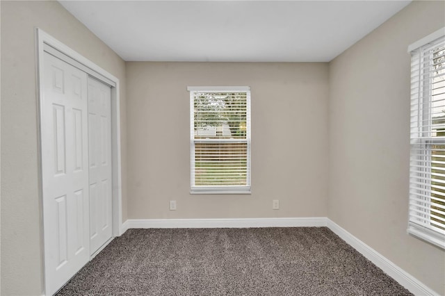 unfurnished bedroom with a closet, multiple windows, and dark colored carpet