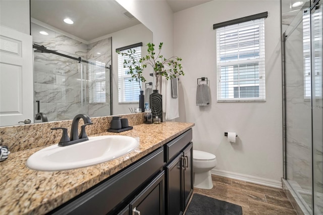 bathroom featuring vanity, a healthy amount of sunlight, a shower with shower door, and toilet