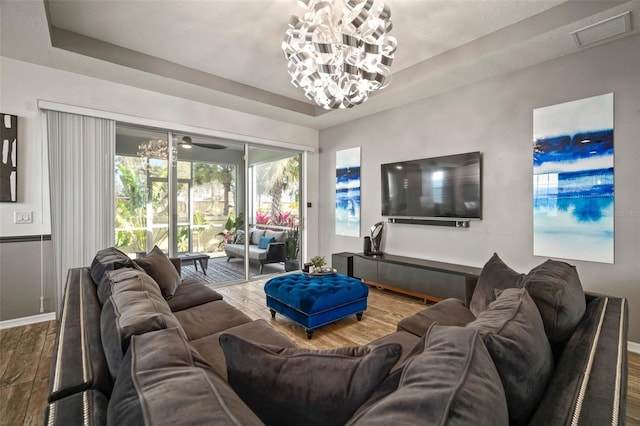 living room featuring a raised ceiling, ceiling fan with notable chandelier, and hardwood / wood-style flooring