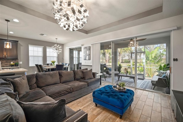 living room featuring a tray ceiling, sink, and an inviting chandelier