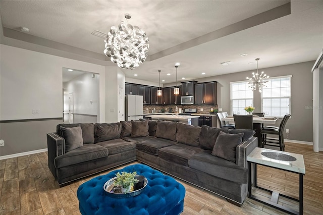 living room with a chandelier, light hardwood / wood-style floors, a raised ceiling, and sink