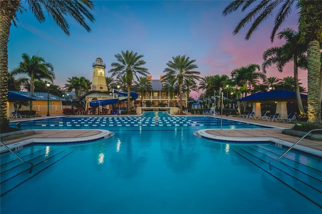 pool at dusk with a patio area and a water slide