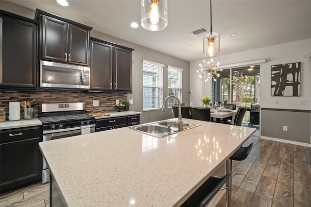 kitchen with decorative light fixtures, sink, stainless steel appliances, and a kitchen island with sink