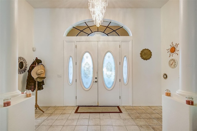 foyer entrance with light tile floors, a notable chandelier, ornate columns, and french doors