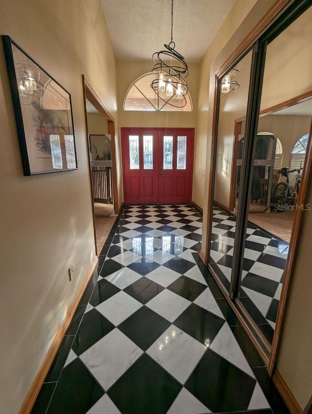 entryway with an inviting chandelier, dark tile floors, a textured ceiling, and a towering ceiling