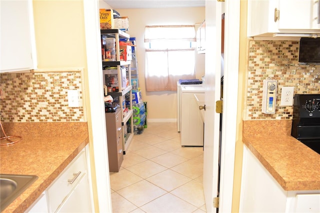 kitchen featuring white cabinetry, backsplash, washing machine and clothes dryer, and light tile flooring