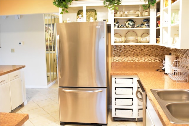 kitchen featuring white cabinets, backsplash, stainless steel refrigerator, and light tile flooring