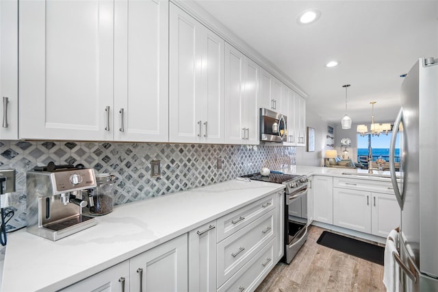 kitchen featuring hanging light fixtures, a notable chandelier, appliances with stainless steel finishes, light hardwood / wood-style floors, and white cabinets