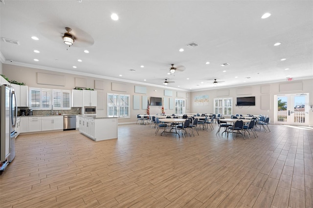 unfurnished living room featuring plenty of natural light, crown molding, ceiling fan, and light wood-type flooring