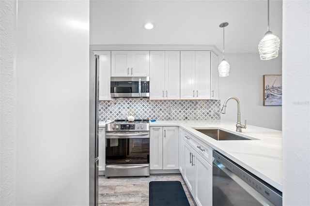 kitchen with hanging light fixtures, sink, light hardwood / wood-style flooring, stainless steel appliances, and white cabinets