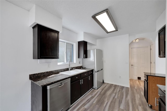 kitchen featuring dark stone counters, stainless steel dishwasher, white refrigerator, light hardwood / wood-style floors, and sink