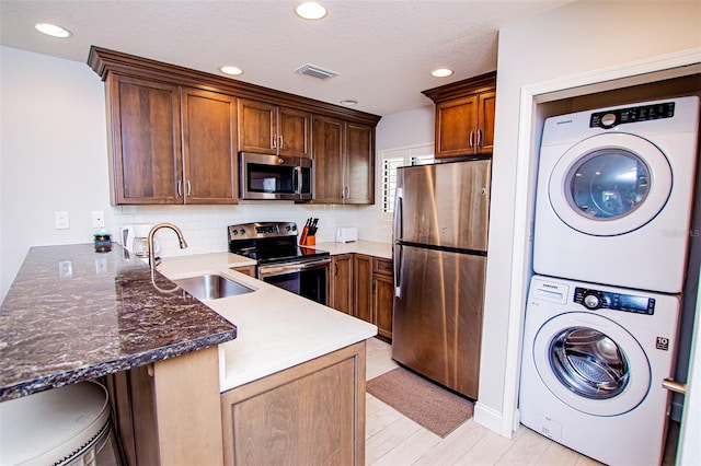 kitchen with stacked washer and clothes dryer, appliances with stainless steel finishes, sink, backsplash, and kitchen peninsula