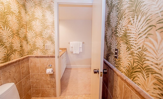 bathroom featuring tile flooring, vanity, toilet, and tile walls