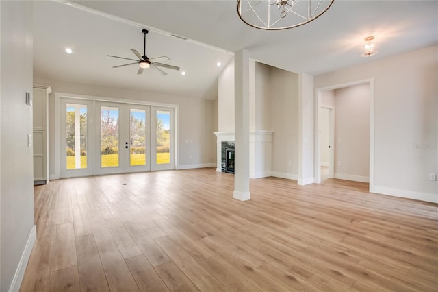 unfurnished living room featuring french doors, lofted ceiling, light hardwood / wood-style floors, and ceiling fan with notable chandelier