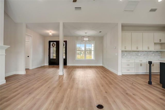 unfurnished living room with an inviting chandelier and light hardwood / wood-style floors