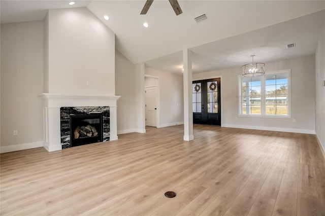 unfurnished living room featuring french doors, a premium fireplace, light hardwood / wood-style floors, vaulted ceiling, and ceiling fan with notable chandelier