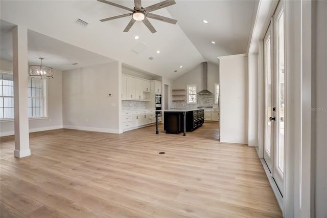 unfurnished living room featuring lofted ceiling, plenty of natural light, light wood-type flooring, and ceiling fan with notable chandelier