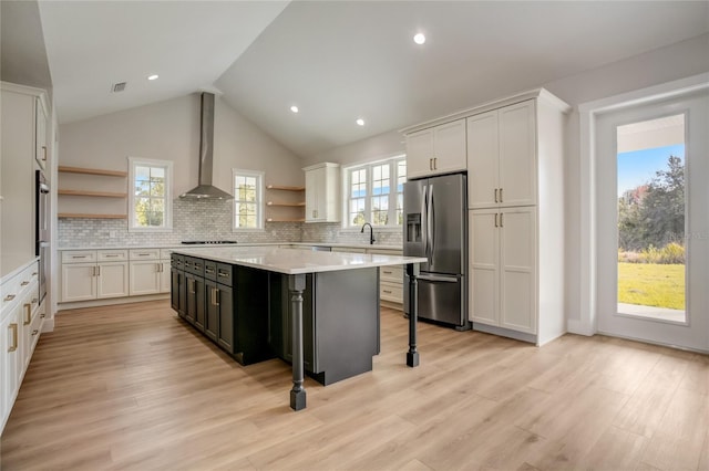 kitchen featuring light hardwood / wood-style floors, a center island, wall chimney range hood, stainless steel fridge with ice dispenser, and white cabinetry