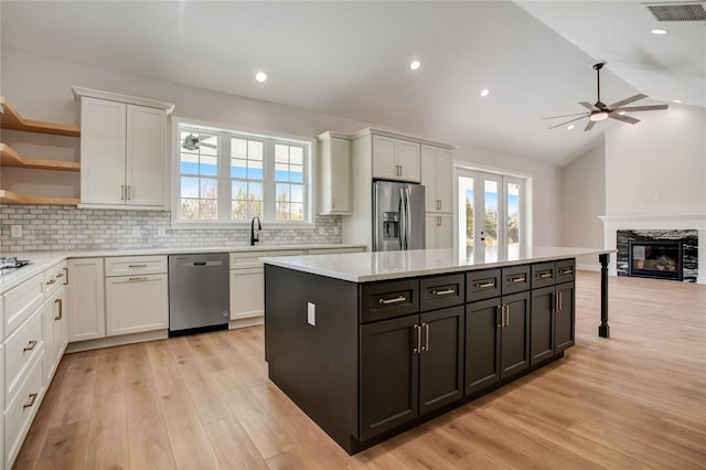 kitchen with stainless steel appliances, a fireplace, vaulted ceiling, and light wood-type flooring