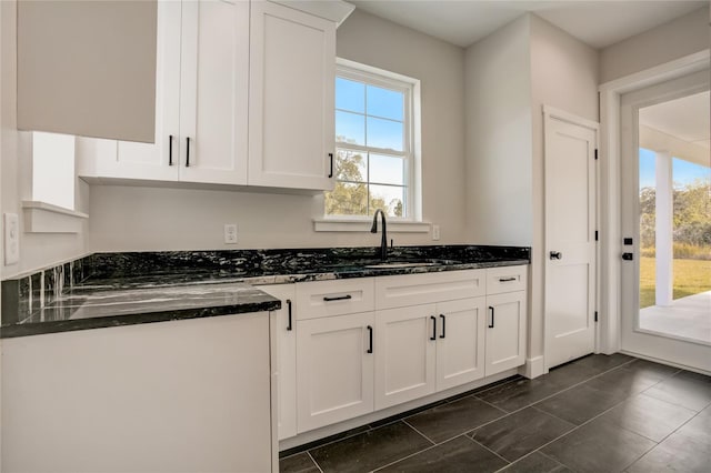 kitchen featuring dark tile floors, white cabinetry, dark stone counters, and sink