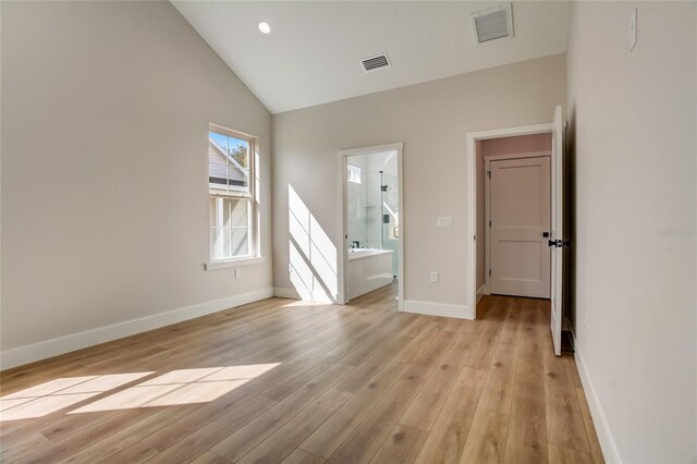 unfurnished bedroom with lofted ceiling, ensuite bathroom, and light wood-type flooring